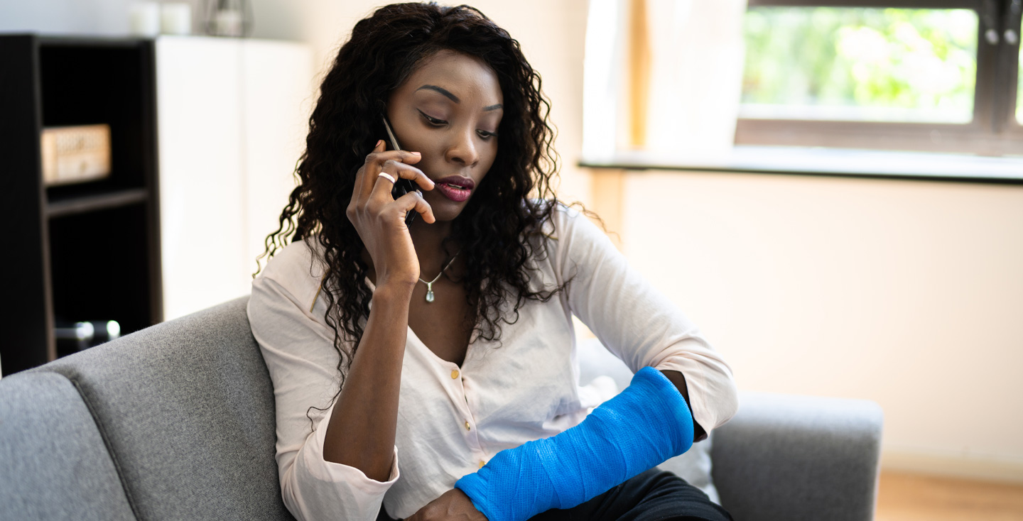 Woman on the phone, looking at a cast on her arm.
